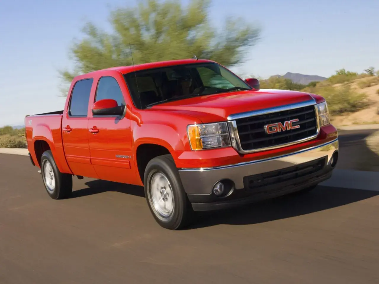 Czerwony pickup GMC Sierra z napędem 4x4 jedzie po pustynnej drodze.