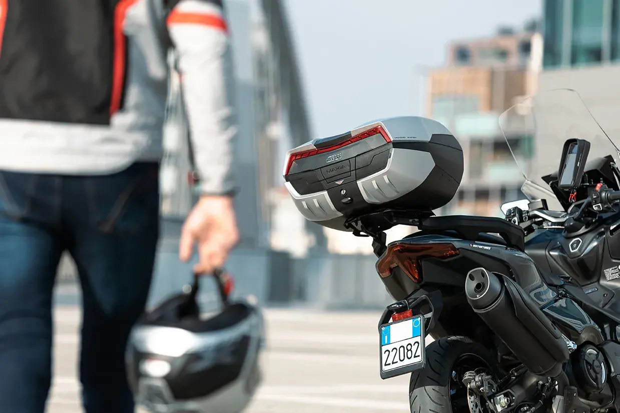 Hombre con casco en mano, listo para llevar su maleta en moto. La moto tiene un top case Givi Maxia.