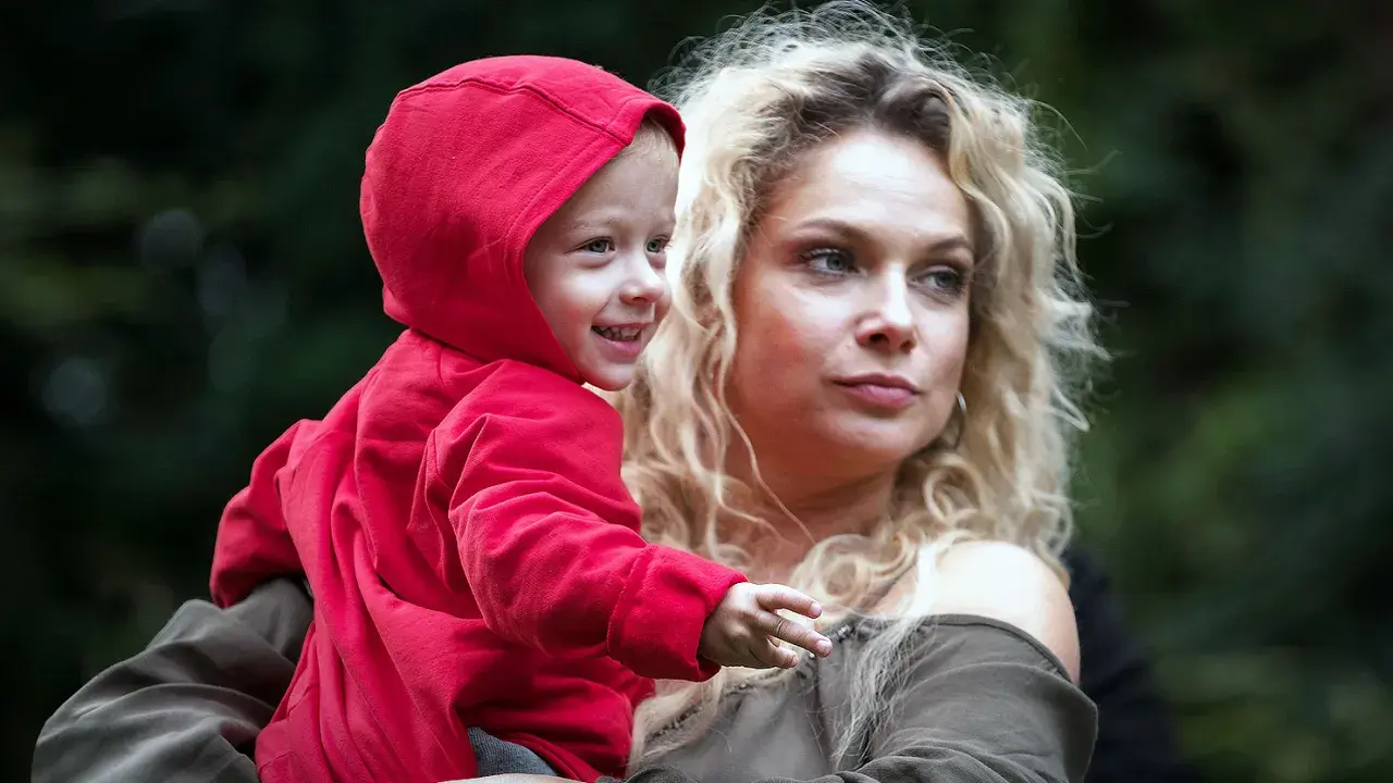 Joanna Liszowska z dziećmi, uśmiechnięty chłopiec w czerwonej bluzie na rękach mamy.
