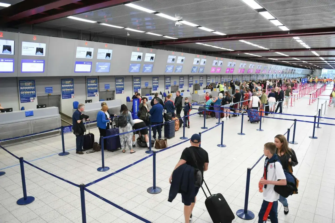 Kolejka do check-in na lotnisku. Pasażerowie z walizkami czekają na obsługę przy stanowiskach odprawy.