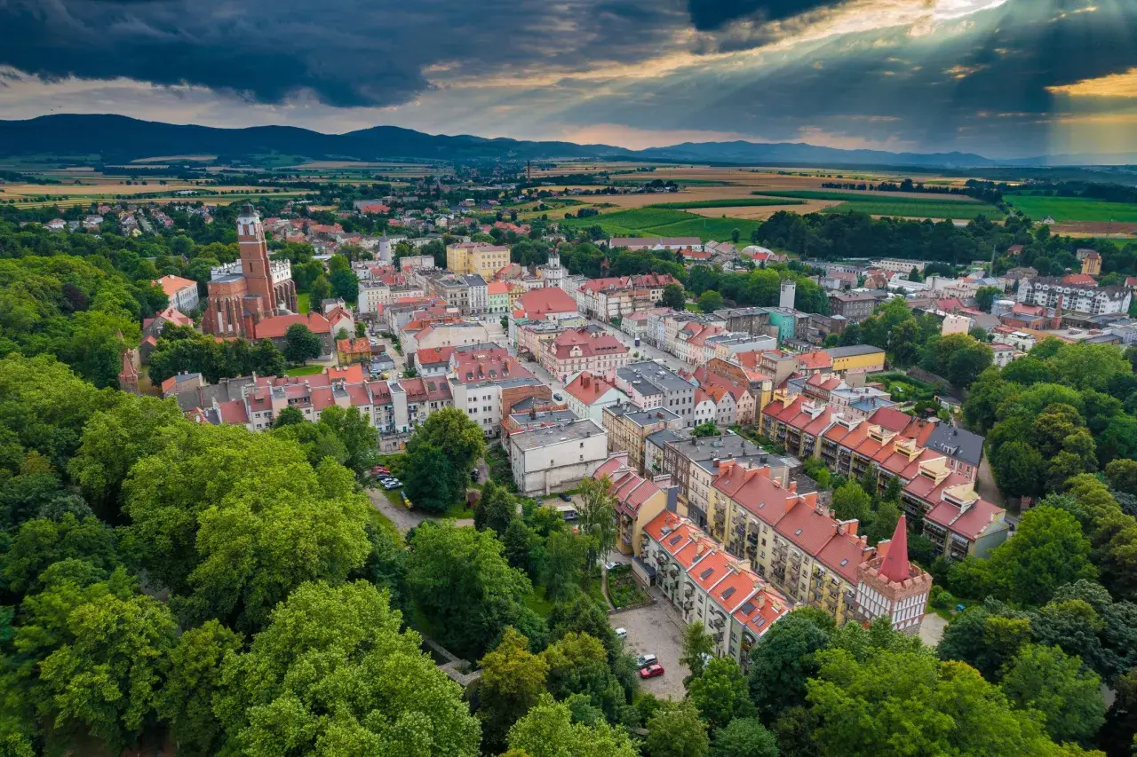 Malownicze polskie Carcassonne z dominującą wieżą kościelną, otoczone zielenią i górami.