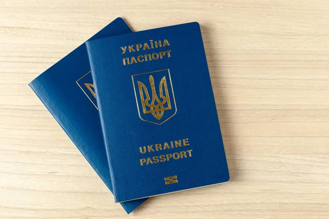 Dwa niebieskie paszporty biometryczne Ukrainy leżą na drewnianym blacie.