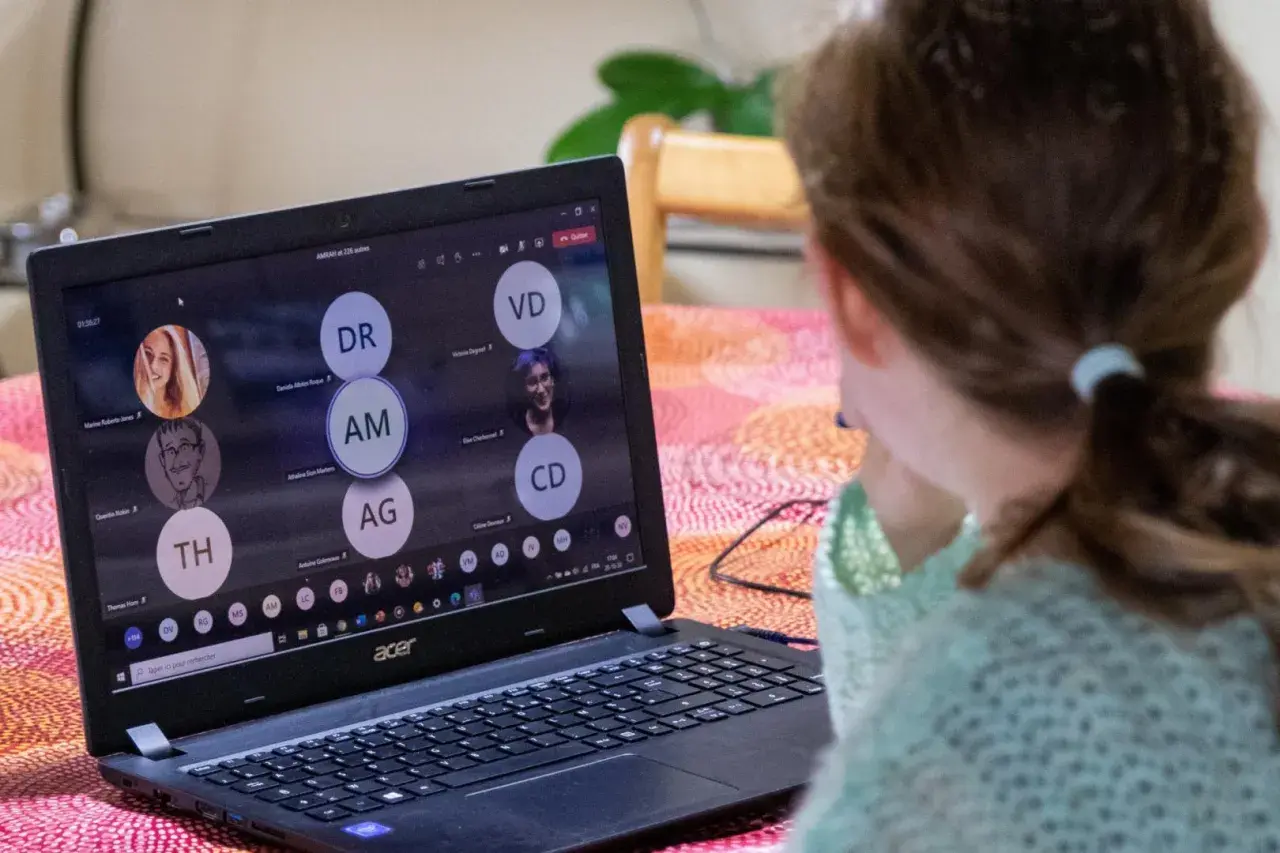 Dziewczynka uczestniczy w lekcji online przez msteams. Na ekranie laptopa widać wiele okręgów z inicjałami uczestników.