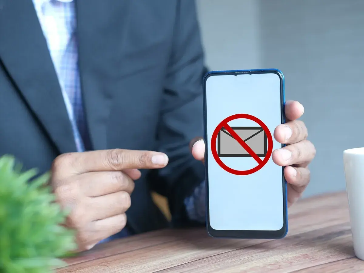 Hombre señala un teléfono con un símbolo de "no" sobre un sobre. Parece que no me llegan los sms.