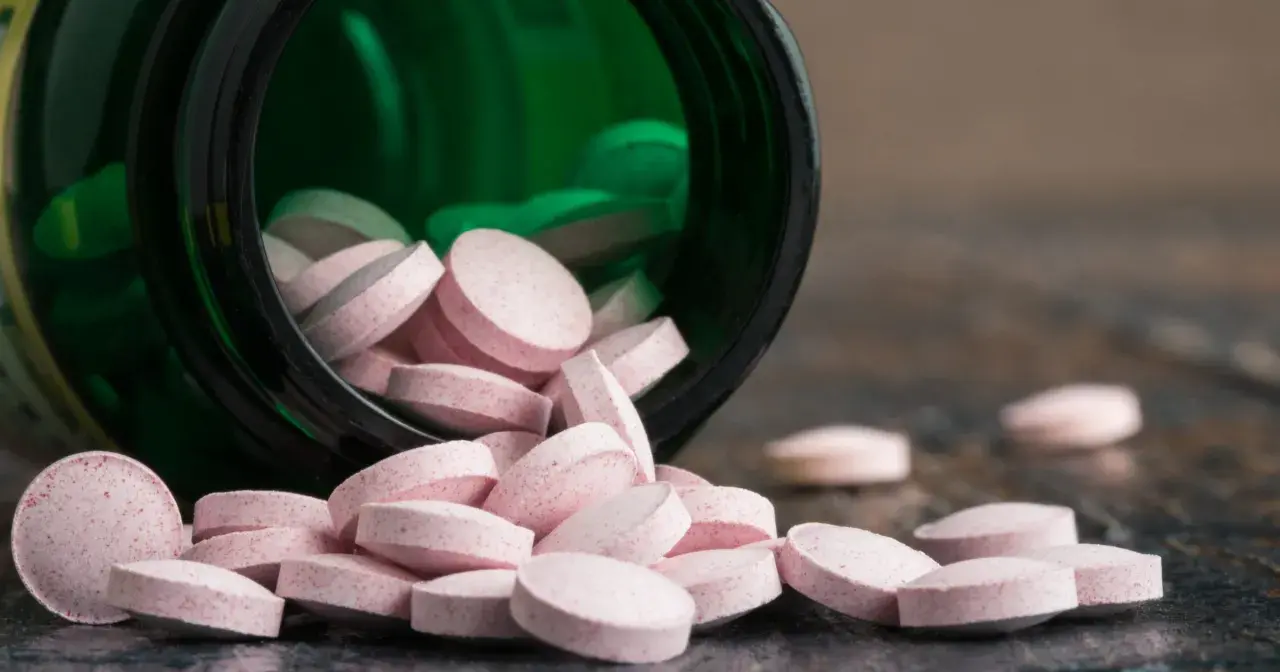 Różowe tabletki wysypują się z zielonego pojemnika. Wśród nich widać tabletki z chromem, które mogą pomóc w utrzymaniu prawidłowego metabolizmu.