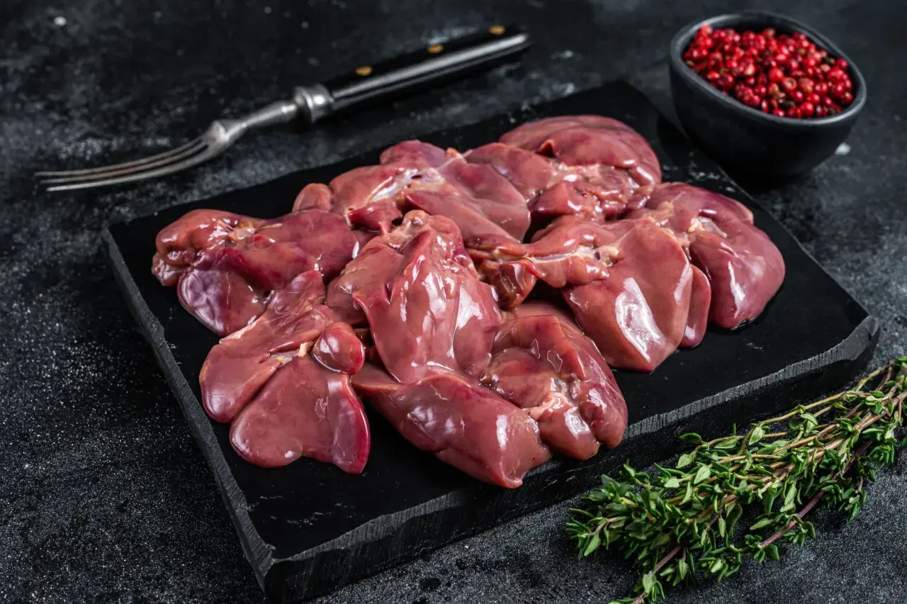 Frische barf innereien, roh und appetitlich auf einem schwarzen Brett, garniert mit Thymian und rosa Pfeffer.