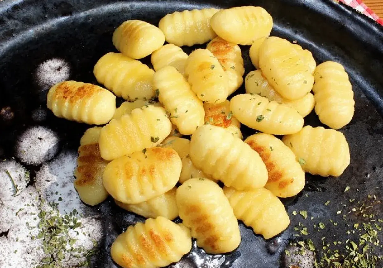 Złociste, domowe **makaron gnocchi** z ziołami, ułożone na ciemnym talerzu.