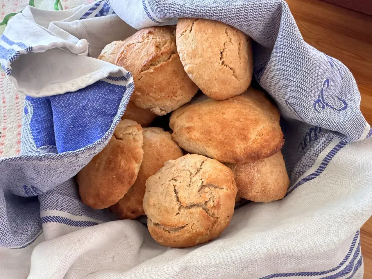 En hög med gyllene, luftiga scones som vilar i en blåvitrandig kökshandduk. Perfekt för fikat!