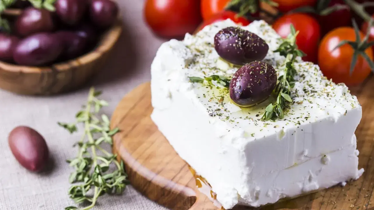 Kostka sera feta, polana oliwą i posypana ziołami, z oliwkami i pomidorkami w tle. Właściwości sera feta doceniane są w kuchni śródziemnomorskiej.
