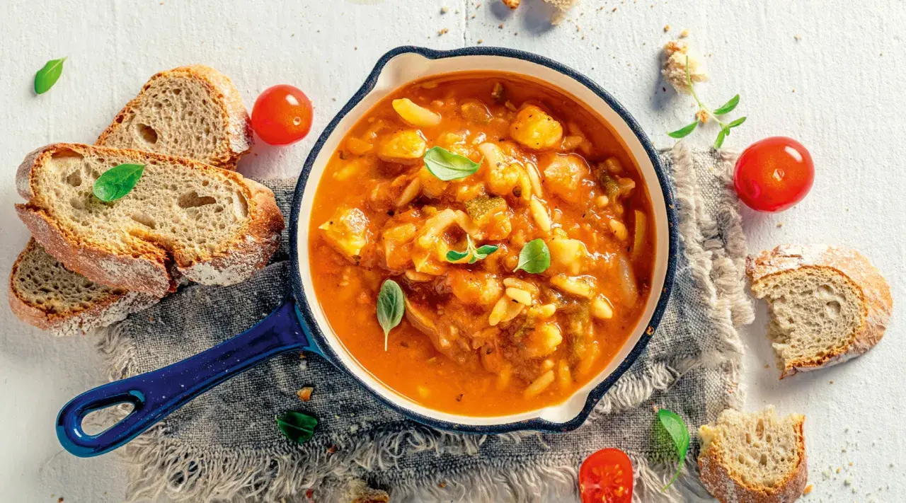 Eine dampfende, traditionelle italienische Suppe mit Gemüse und Pasta, serviert mit frischem Brot und Tomaten.
