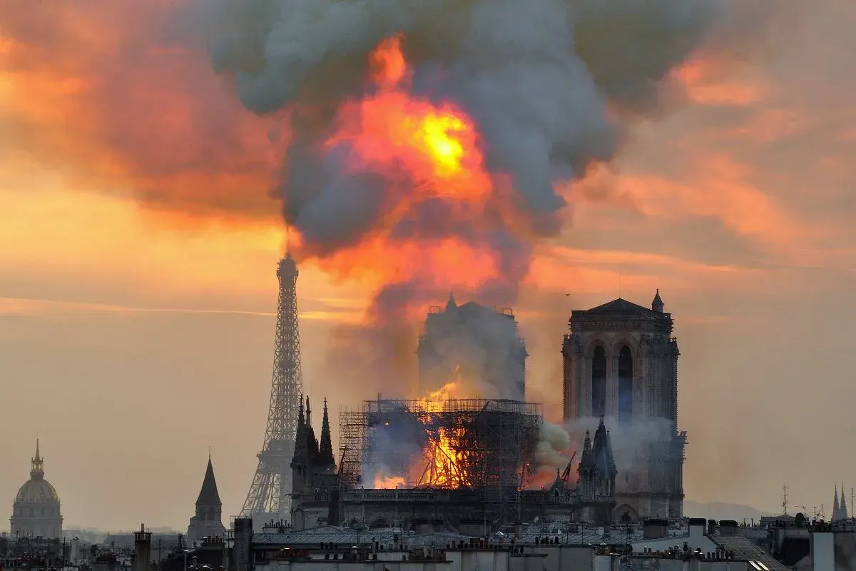Płonąca katedra Notre-Dame w Paryżu z Wieżą Eiffla w tle.
