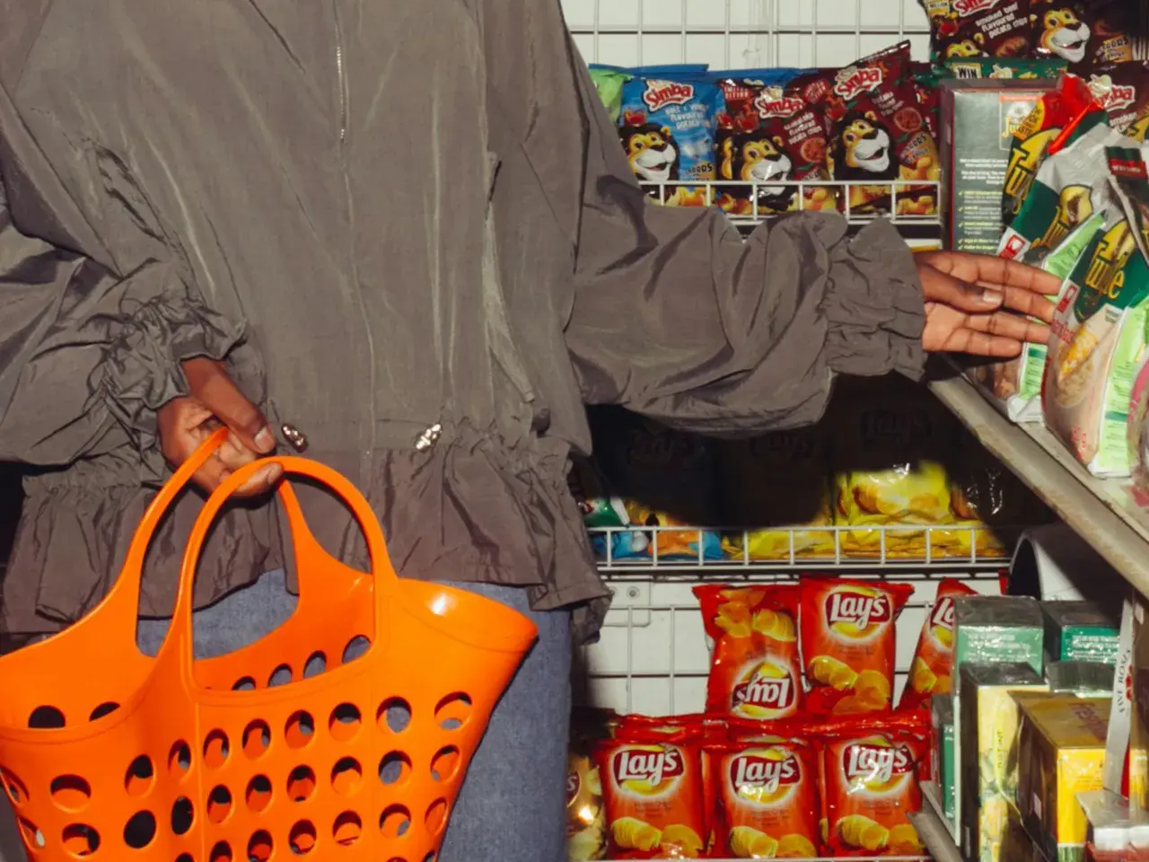 Person mit Einkaufskorb vor Chipsregal. Die **skimpflation definition** zeigt, wie Hersteller bei gleichbleibenden Preisen die Menge reduzieren.