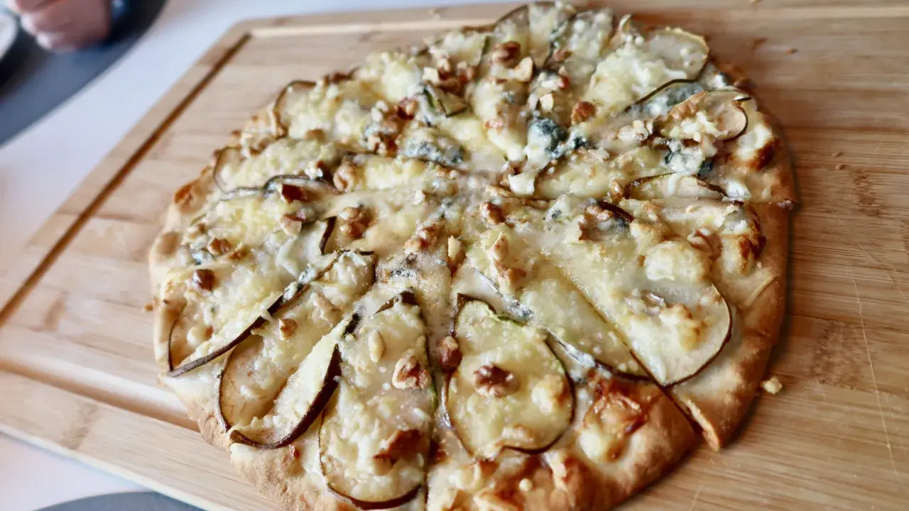 En utsökt pizza med päron, valnötter och krämig gorgonzola på en träskärbräda.