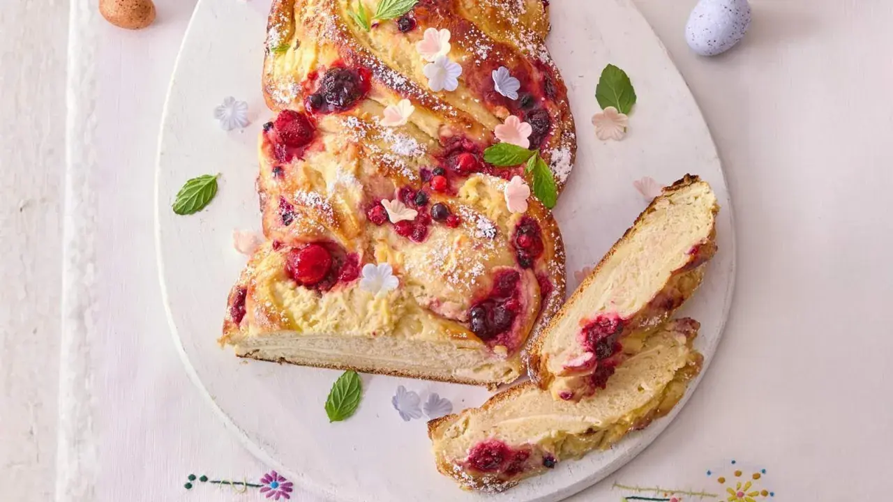 Ein köstlicher Osterzopf mit Quark und Beeren, bestäubt mit Puderzucker und verziert mit Minze und kleinen Blüten.