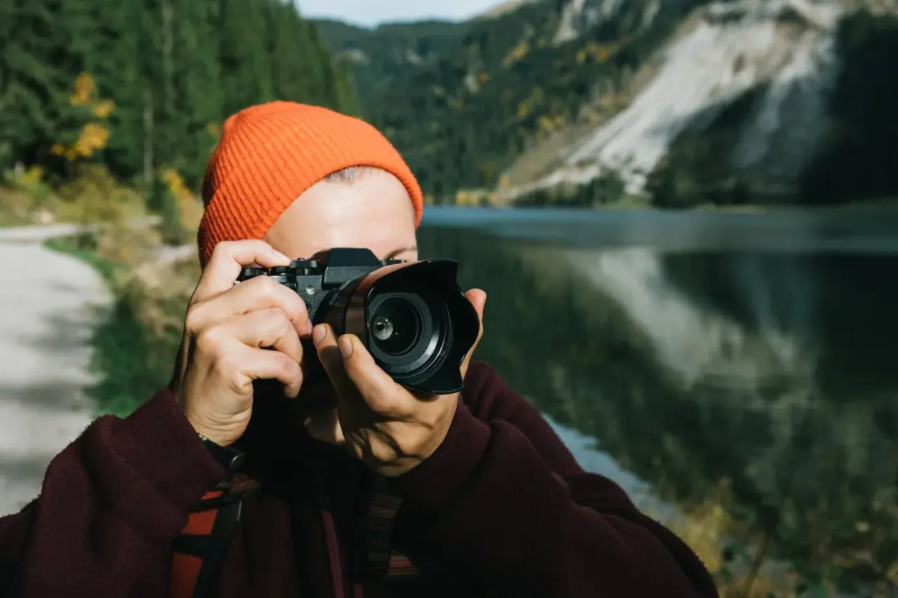 Osoba w pomarańczowej czapce robi zdjęcie aparatem, który mógłby być Nikon D7000. Dane techniczne tego modelu pozwalają na uchwycenie piękna górskiego krajobrazu.