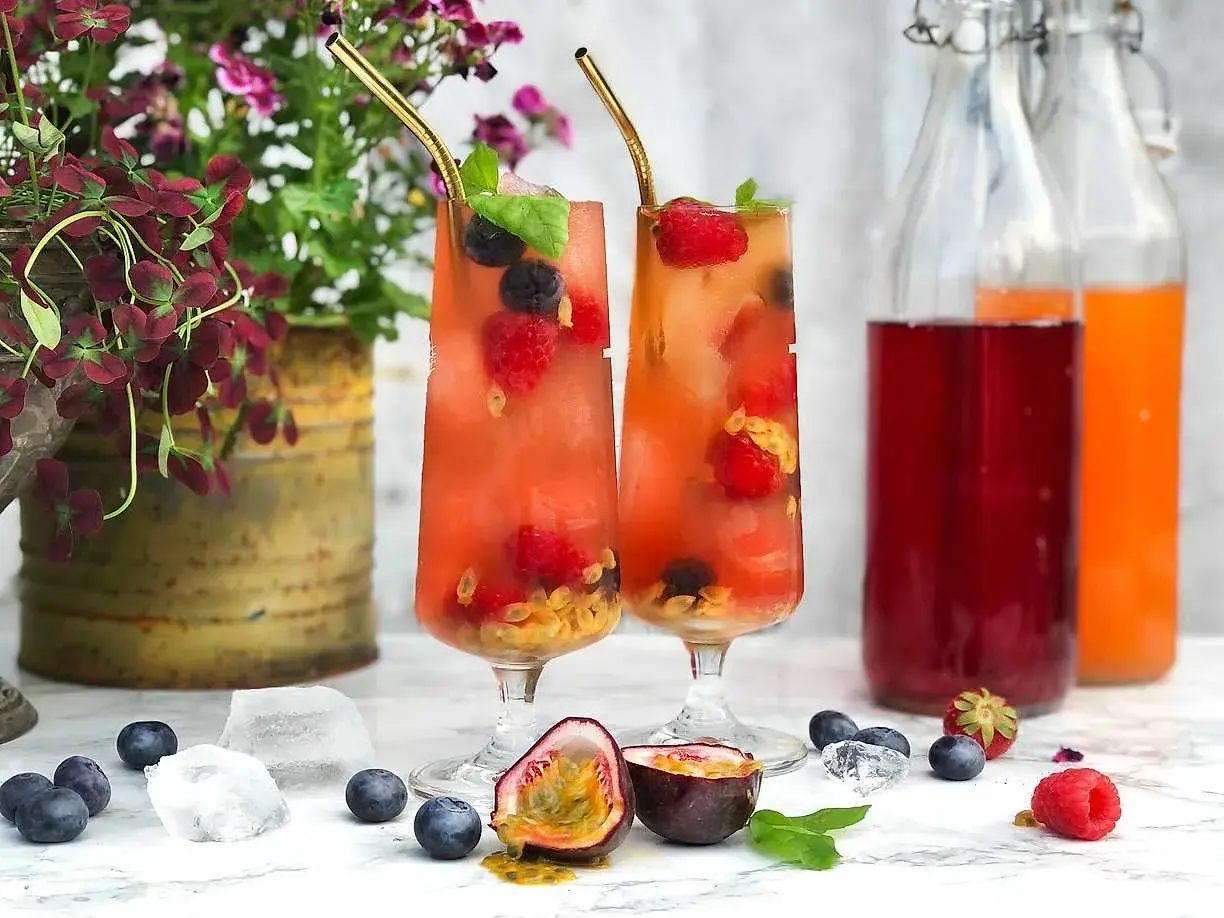 Två glas med fruktiga drinkar, fyllda med bär och passionsfrukt. Perfekt för en somrig bål med bubbel.
