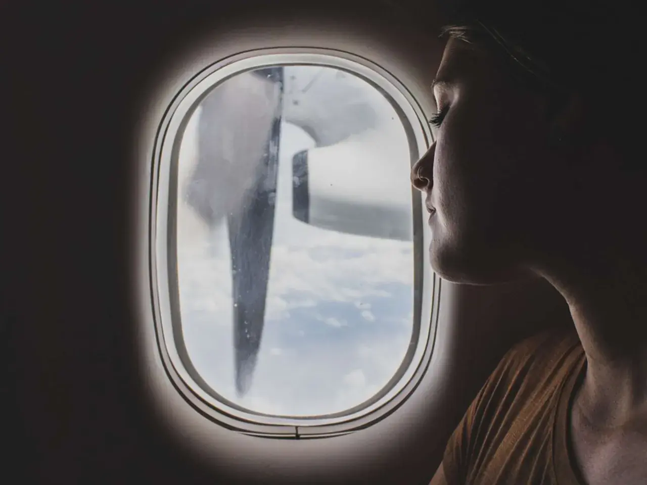 Frau blickt aus dem Flugzeugfenster, während das Flugzeug turbulenzen extrem durchfliegt. Wolken und ein Propeller sind sichtbar.