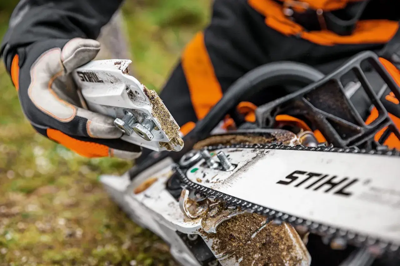 Persona con guantes realiza mantenimiento de motosierra, ajustando piezas cubiertas de serrín.