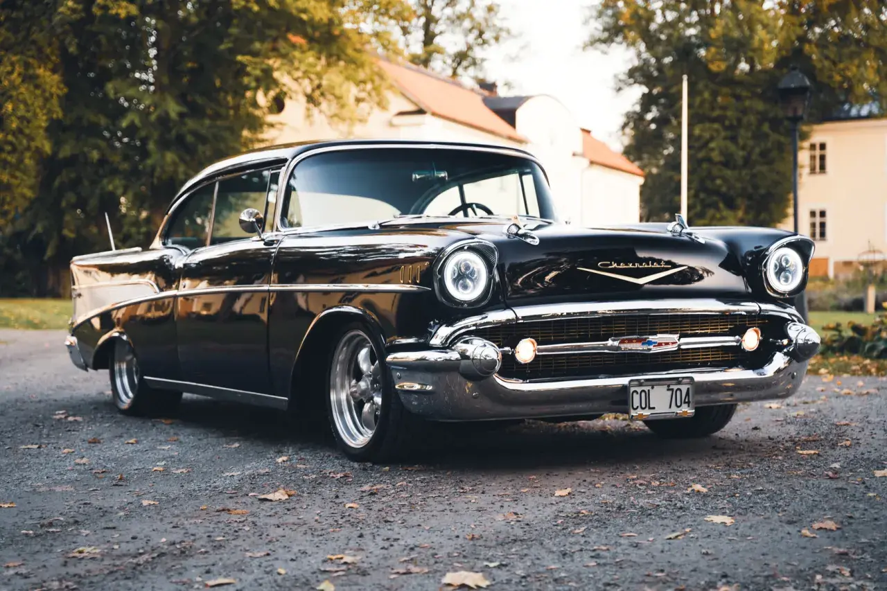 Svart Chevrolet Bel Air bil från 1957 parkerad på grusväg med höstlöv.