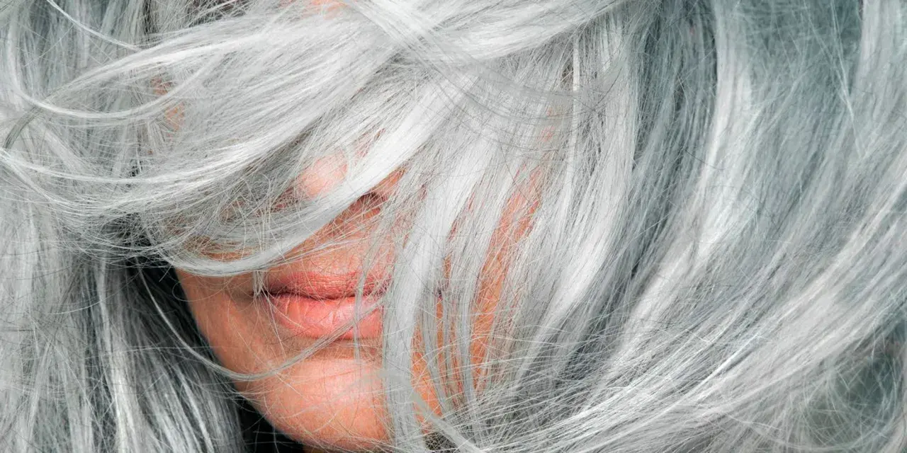 Mechas en pelo blanco natural, cubriendo parte del rostro y labios.