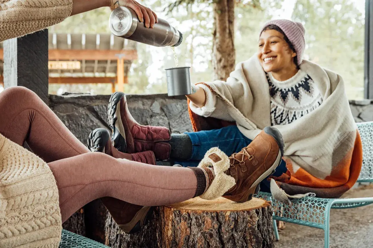 Cozy friends share drinks outdoors, their feet snug in warm shoes to keep feet warm.