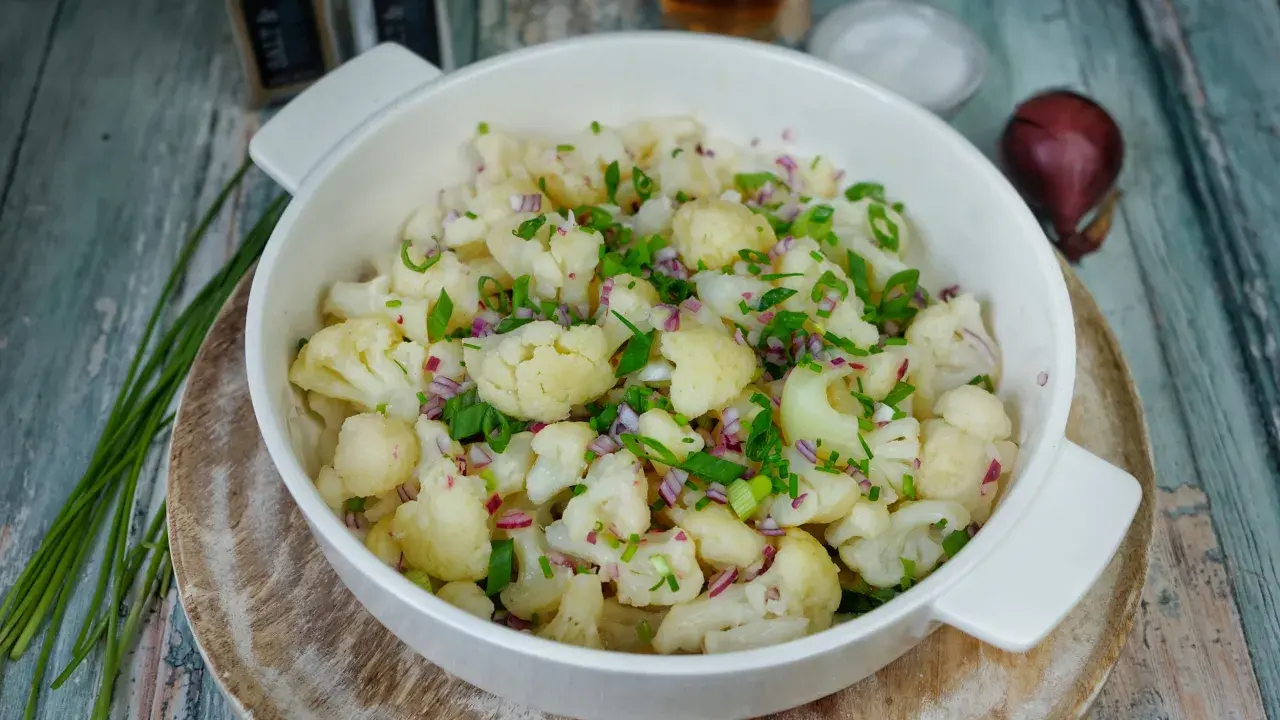 Frischer blumenkohl salat mit roten Zwiebeln und Schnittlauch, serviert in einer weißen Schüssel auf rustikalem Holz.