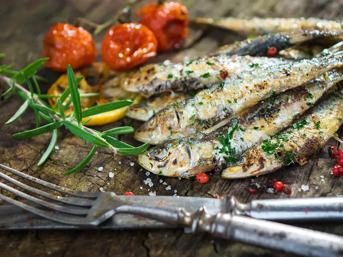 Délicieuses sardines à la plancha, parsemées d'herbes fraîches, accompagnées de tomates cerises rôties et d'une branche de romarin sur fond de bois rustique.
