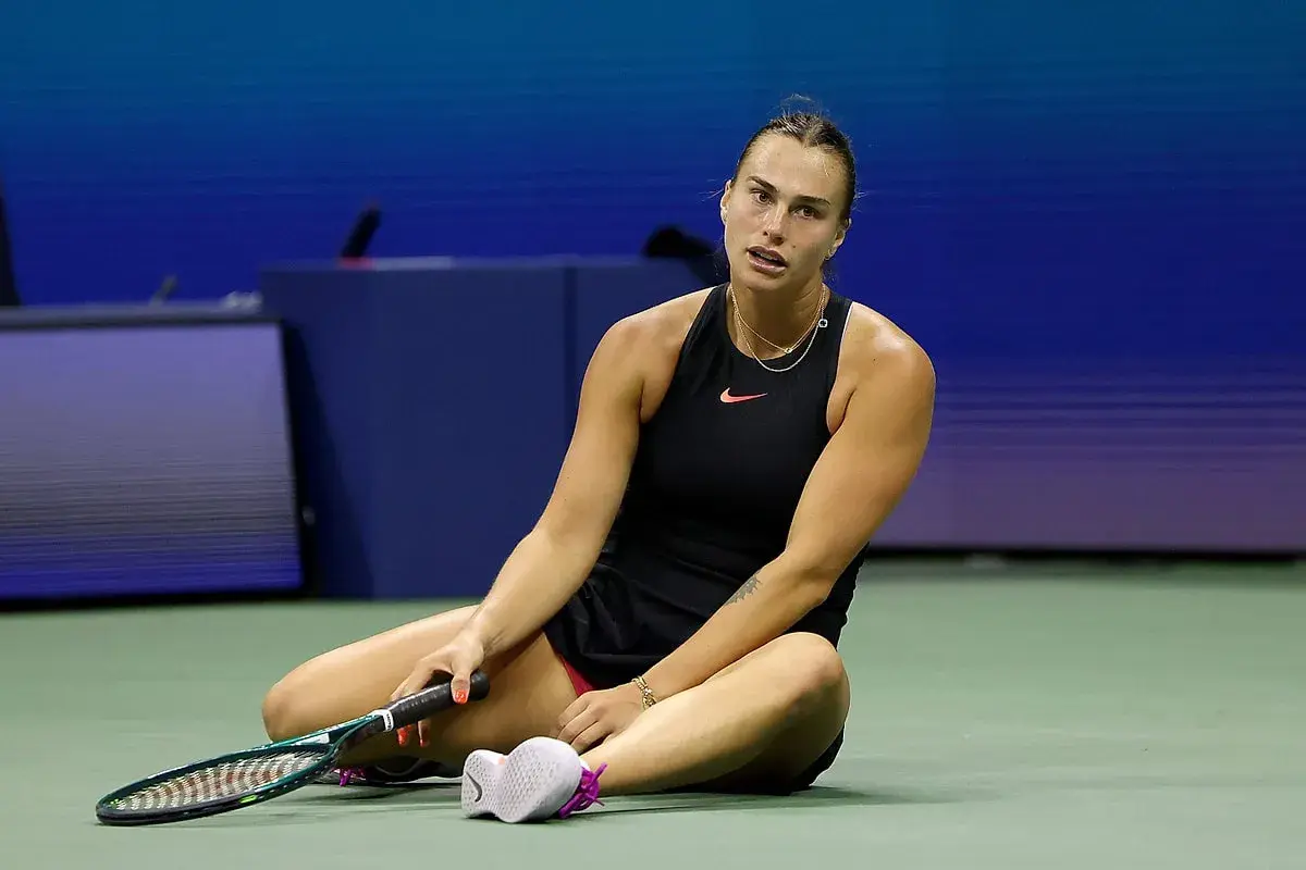 Zmęczona tenisistka siedzi na korcie, trzymając rakietę. Intensywny mecz tenis kobiet.