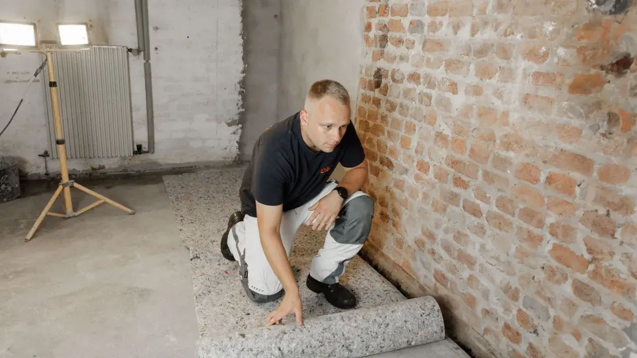 Mann verlegt Dämmmaterial auf dem Boden im Keller, um den **bodenbelag keller feucht** zu schützen.