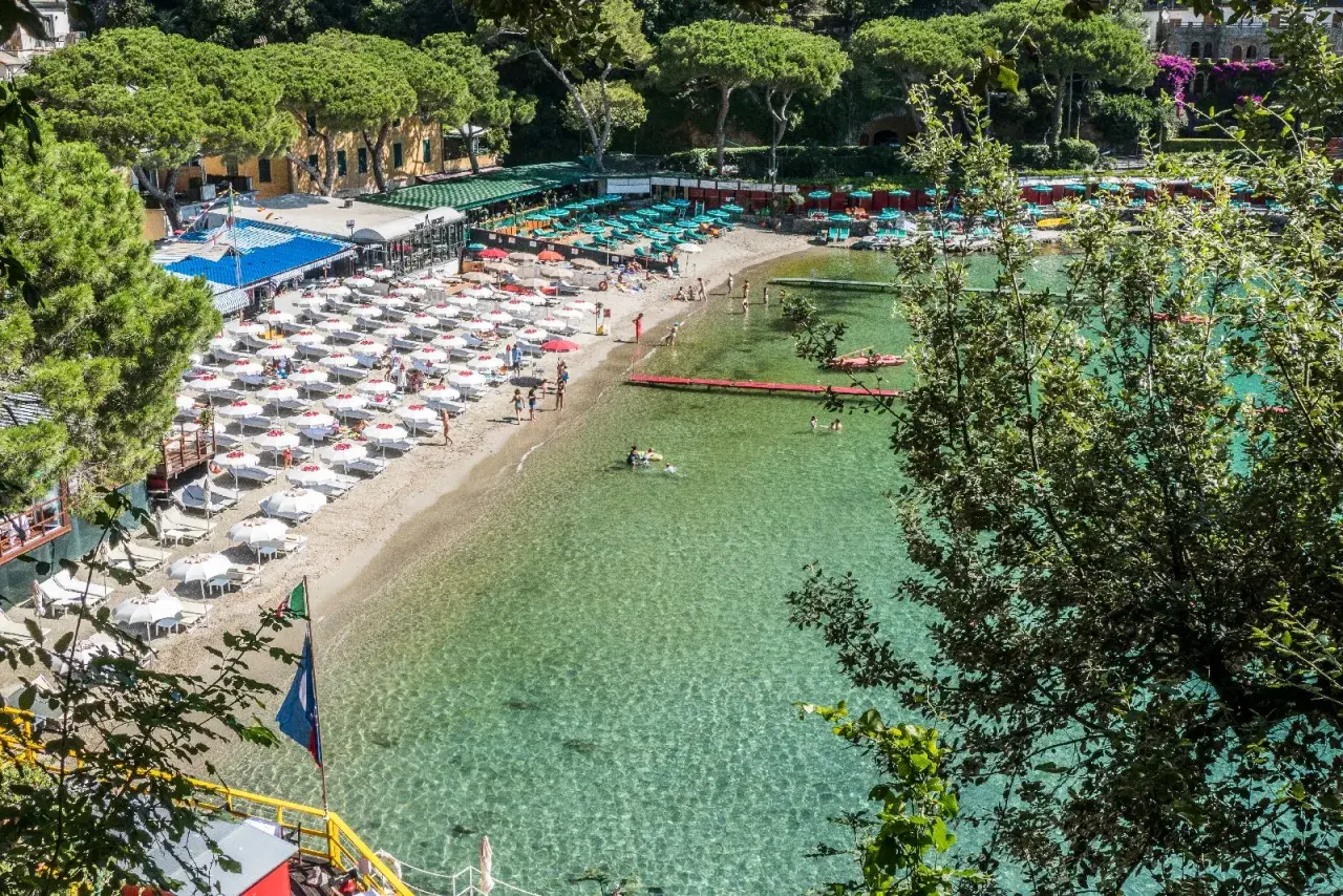 Plage animée d'une ville de la Riviera italienne, avec des parasols blancs, des chaises longues et des baigneurs dans l'eau cristalline.