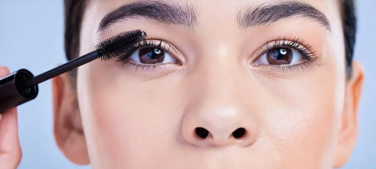 Eine Hand trägt Mascara auf die Wimpern auf, um runde Augen zu schminken.