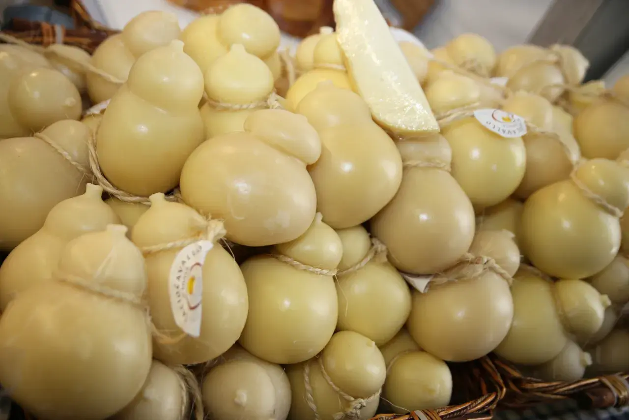 Un cesto pieno di formaggio podolico, alcuni a forma di pera, legati con spago. Un pezzo di formaggio è appoggiato sopra.