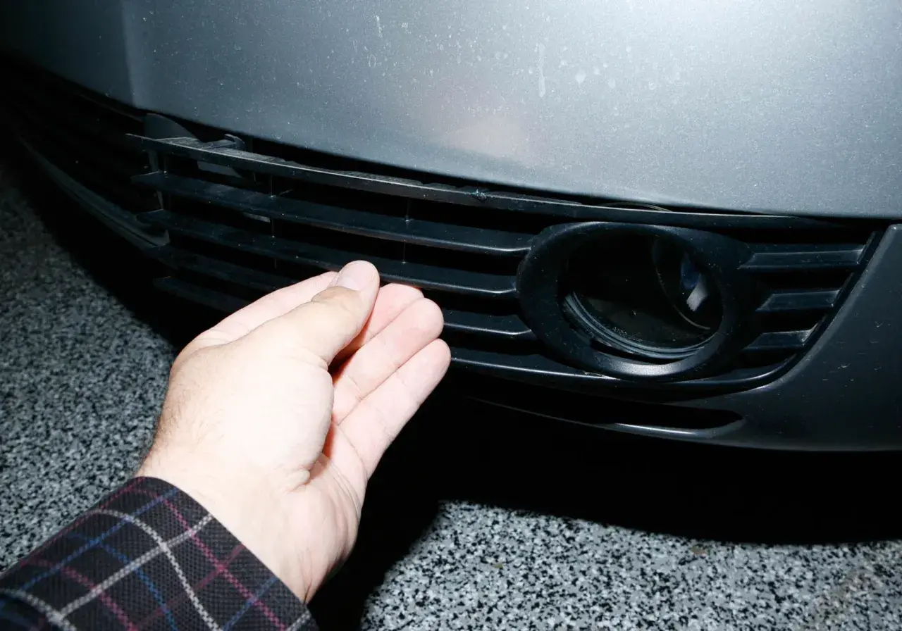 Dłoń naciska na kratkę zderzaka Audi A6 C5, obok otworu na światło przeciwmgielne.