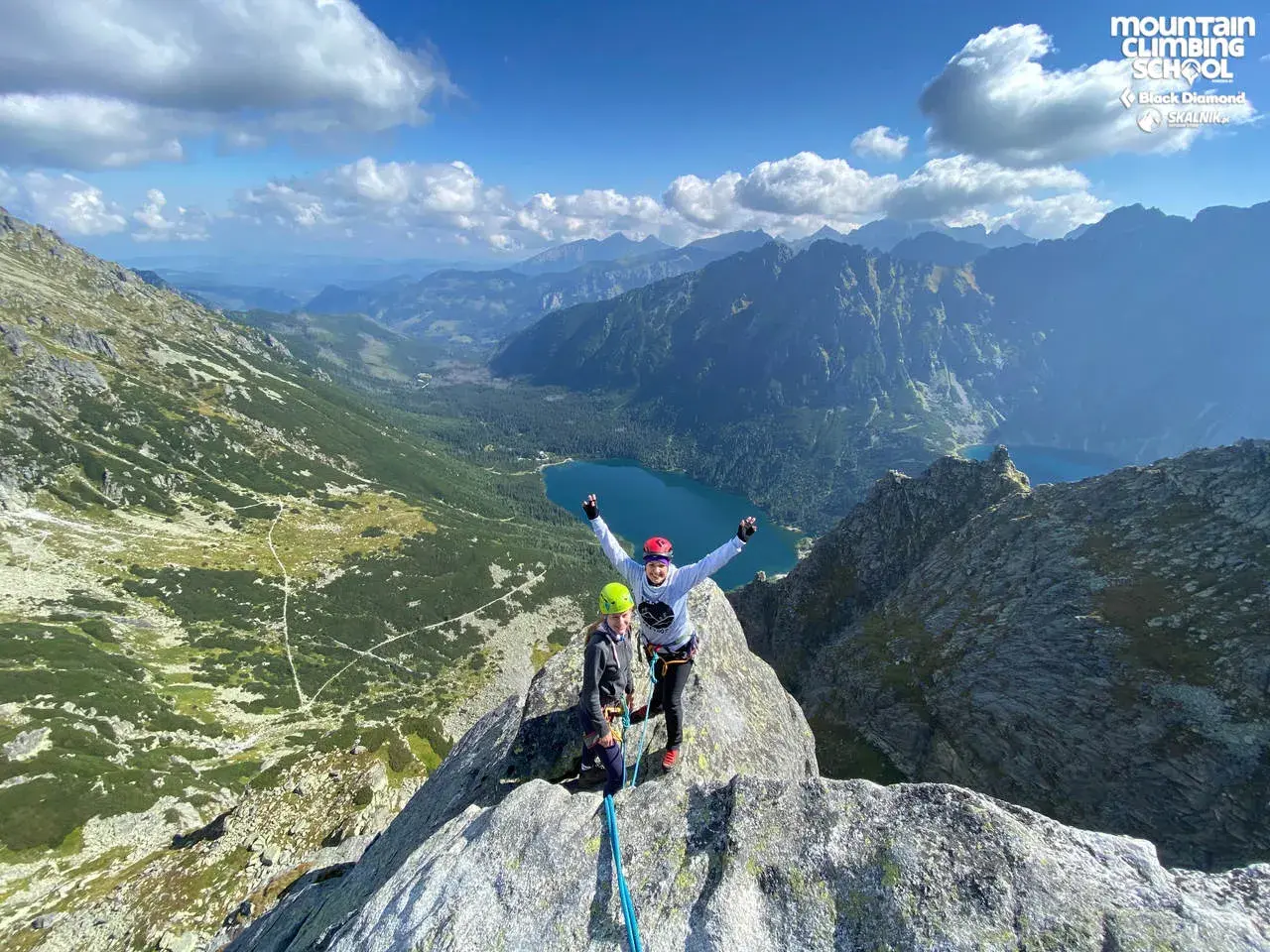 Dwóch wspinaczy na szczycie, radość po udanej wspinaczce. W tle malownicze Tatry i jezioro.