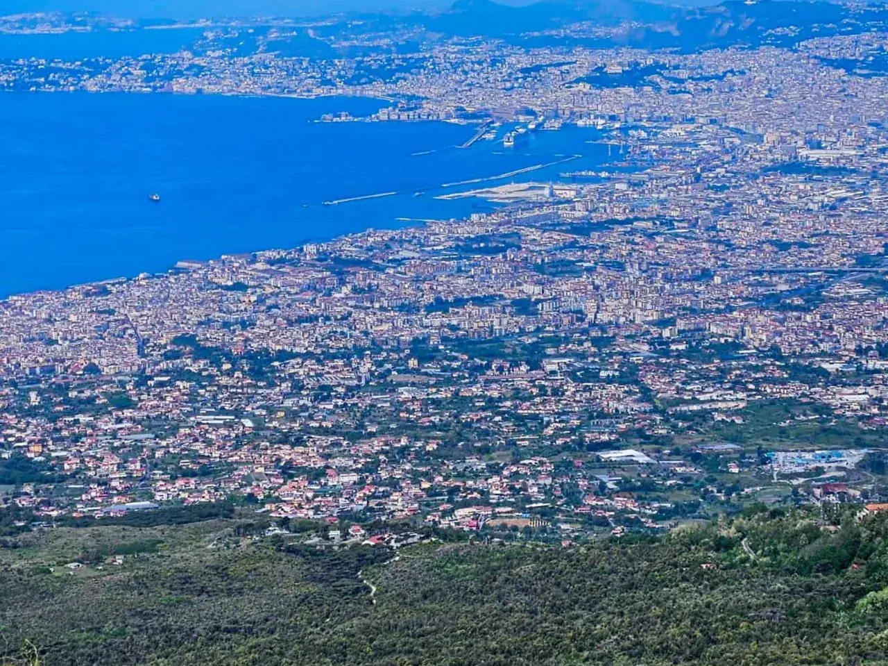 Blick über die weitläufige Stadt Neapel, Italien, mit dem blauen Meer und dem Hafen im Hintergrund.