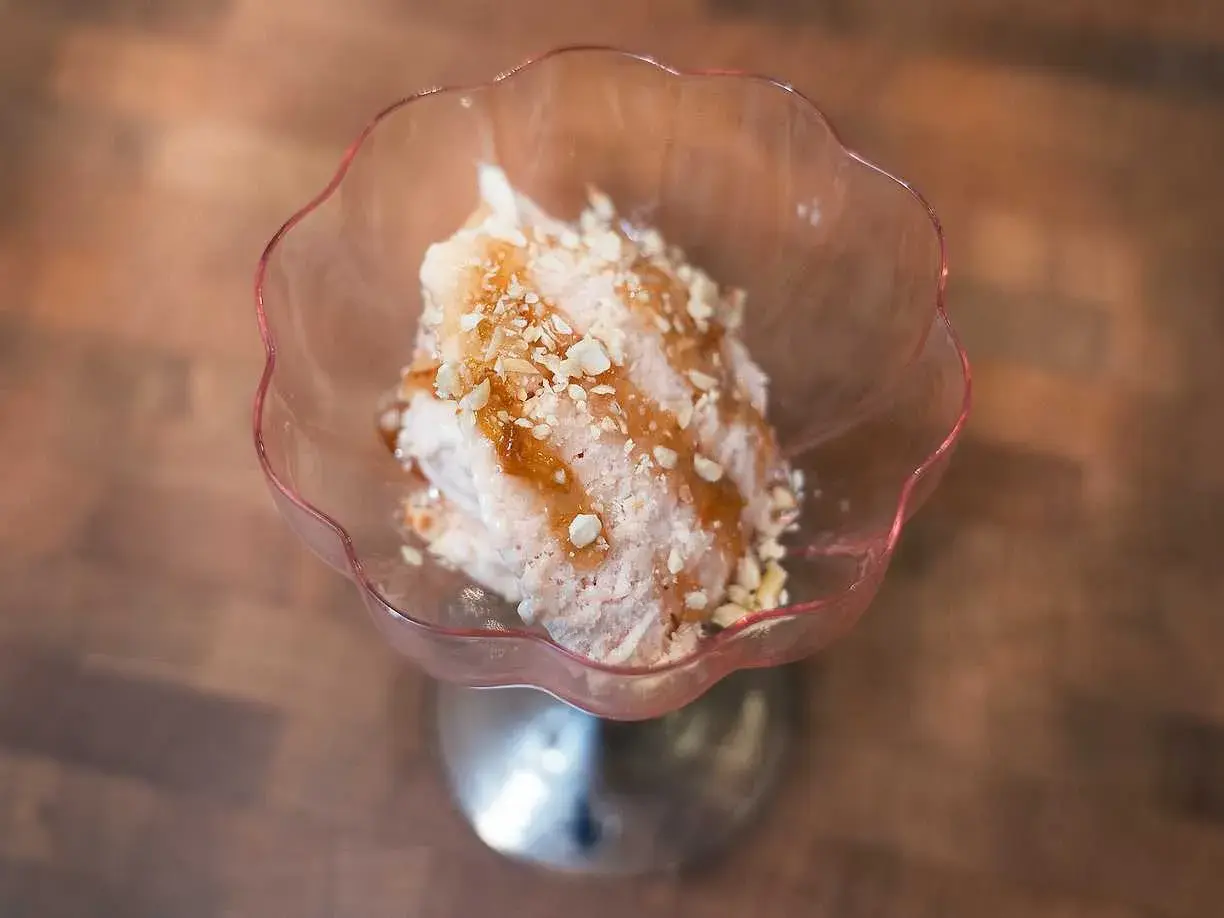 En skål med rosa rabarbersorbet toppad med nötter och sirap. En härlig sommardessert.