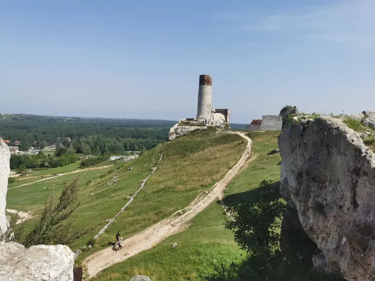 Ruiny zamku na wzgórzu, z wieżą i fragmentami murów. W dole ścieżka, idealna na rowerowe wycieczki po okolicach Częstochowy.