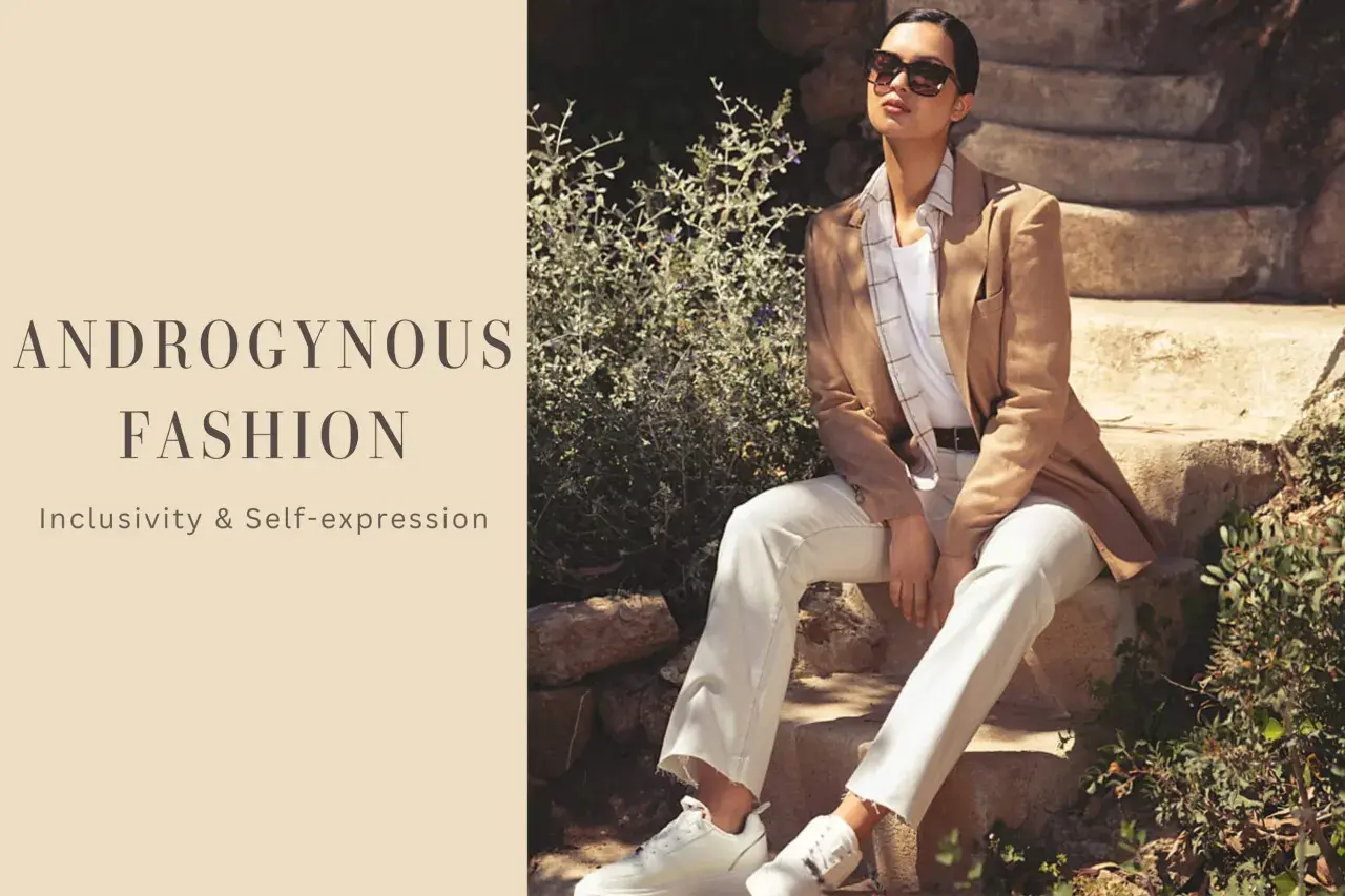 Modello androgino con blazer cammello, pantaloni bianchi e sneakers, su gradini di pietra.