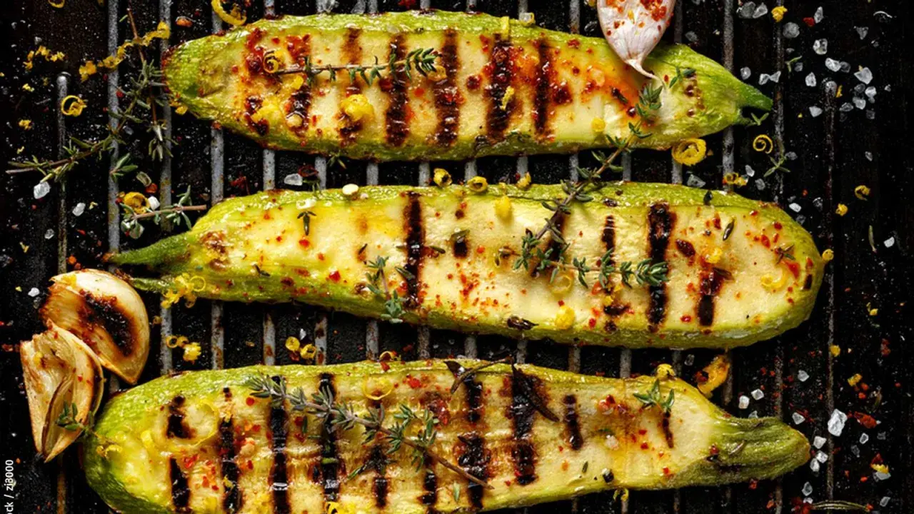Drei perfekt gegrillte Zucchinischiffchen mit Kräutern und Gewürzen auf einem Grillrost. Ein Genuss für Augen und Gaumen!