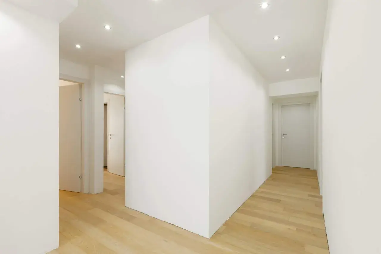 Un corridoio moderno con pavimenti in legno chiaro e una parete in cartongesso curvo che crea un effetto dinamico.