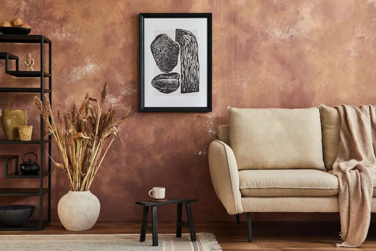 Rusty, textured wall – świetny pomysł co na ścianę zamiast farby. Obok kanapa, grafika i suszone trawy.