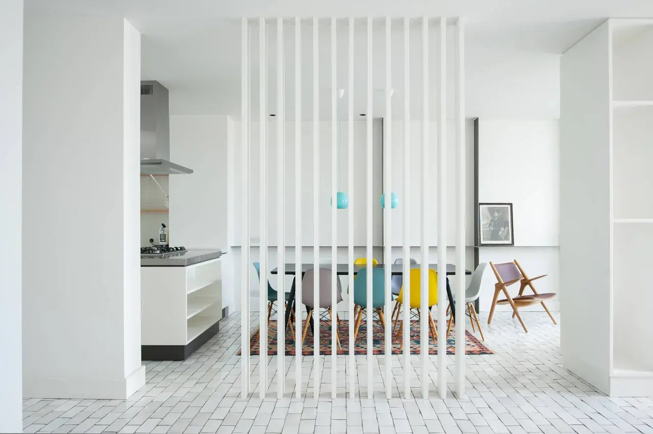 Un divisorio a listelli bianchi separa la cucina moderna da una zona pranzo con sedie colorate. Un'idea per come riempire spazio tra cucina e muro.