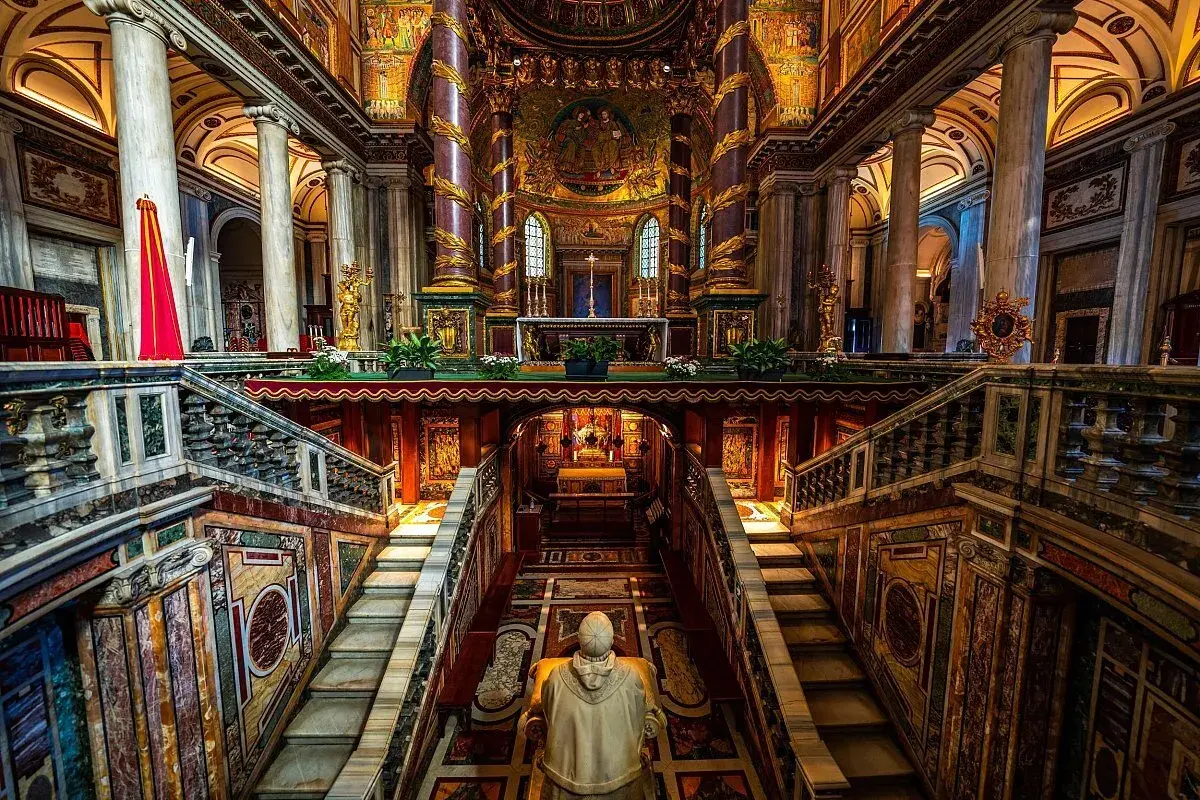 Interno della chiesa San Pietro a Roma, con scale marmoree, mosaici dorati e un altare imponente.