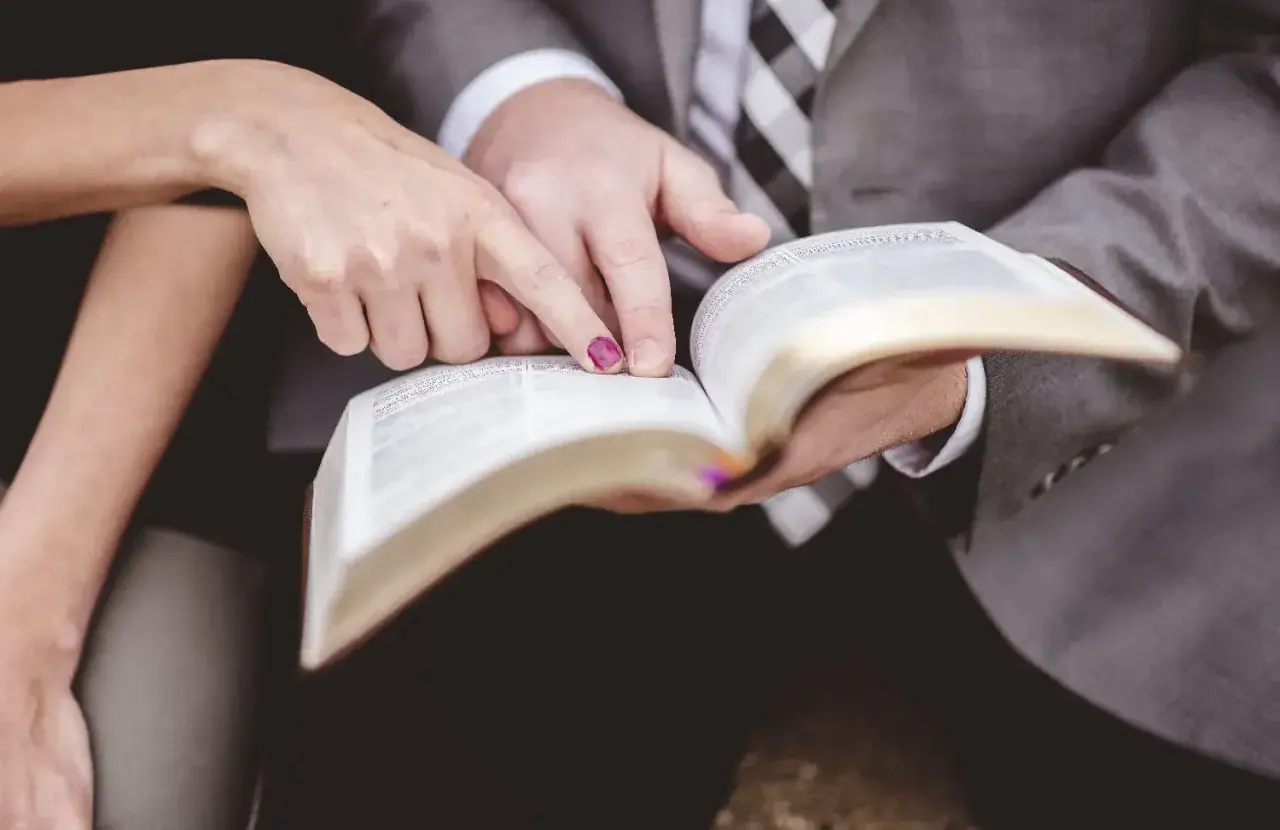 Dłonie pary wskazują na tekst w Biblii, symbolizując wspólną drogę i ewangelia na ślub.