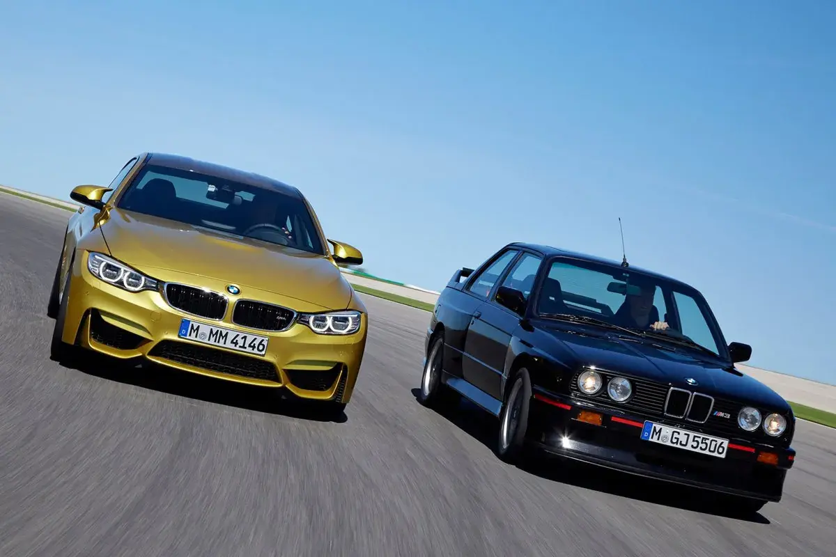 Goldener BMW M4 F80 und schwarzer BMW E30 M3 auf Rennstrecke.