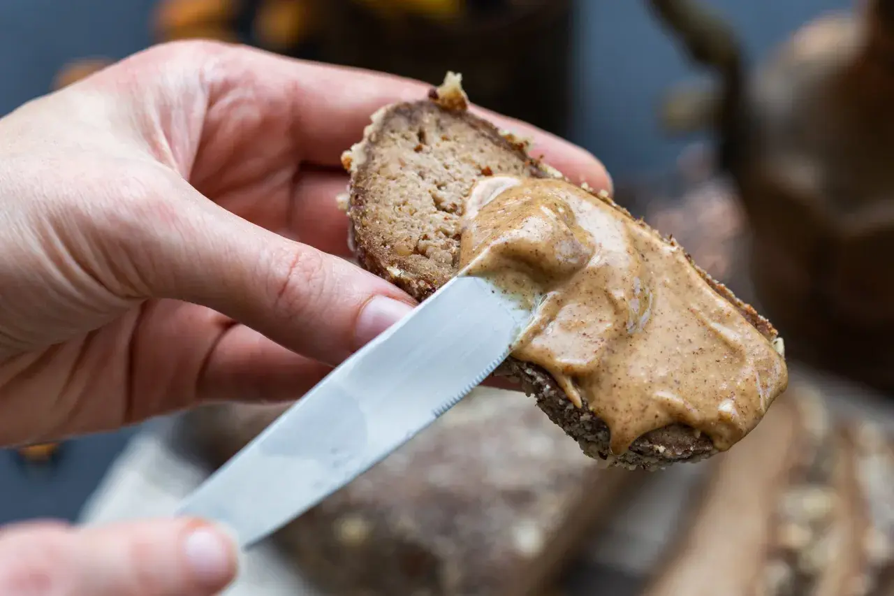 Mano spalma crema di nocciole su pane integrale. Ottima per conoscere i crema di nocciole valori nutrizionali.
