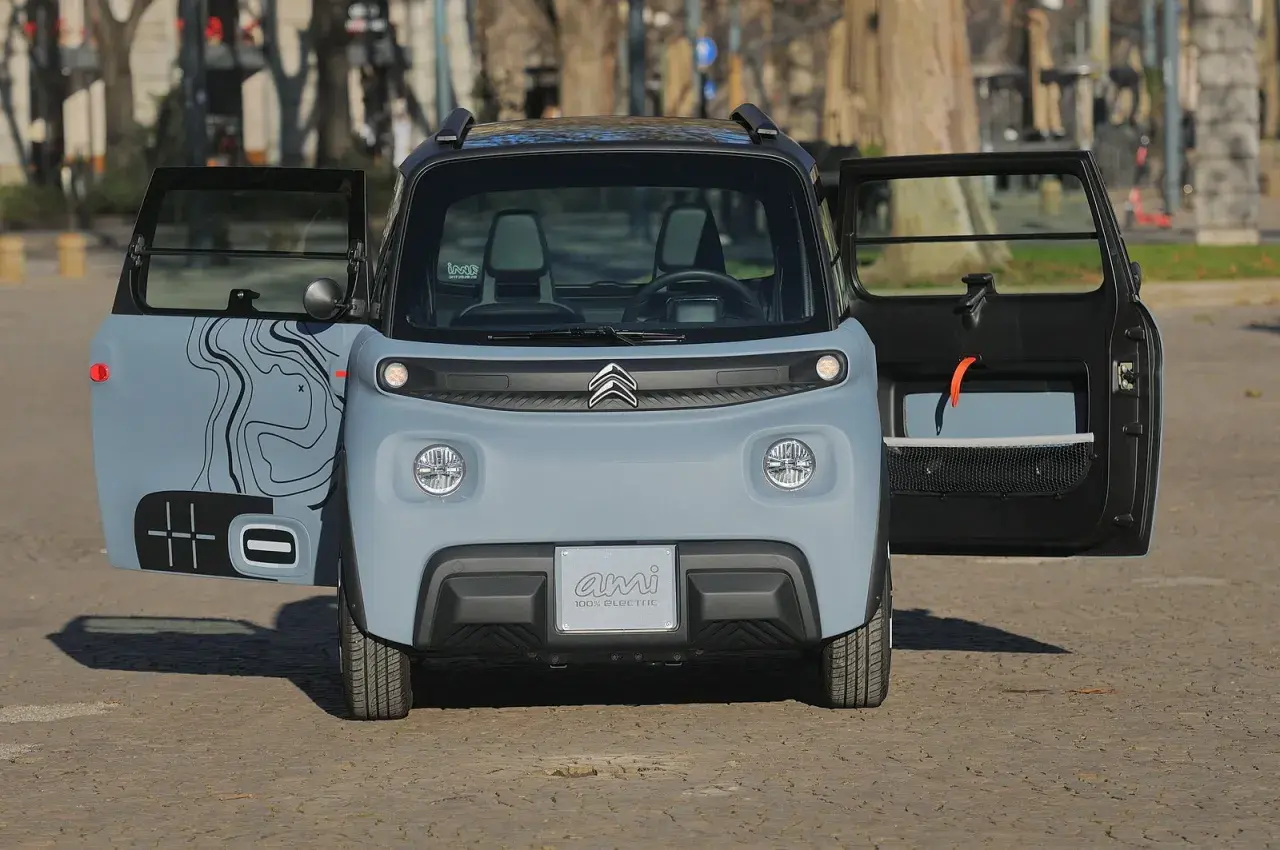 Citroën Ami 100% Electric, in prova, con portiere aperte e grafica stilizzata.