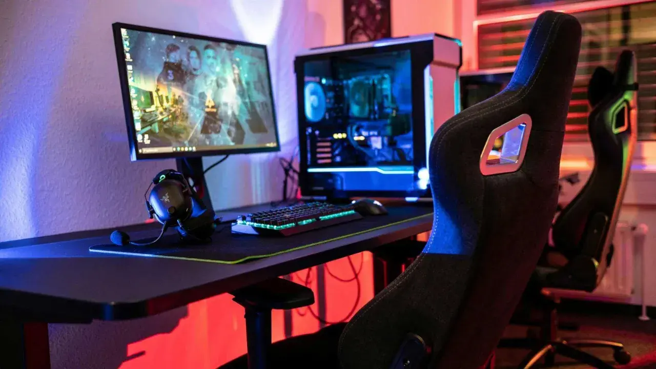 Gaming-Setup mit beleuchtetem PC, Tastatur und Kopfhörern. Der **Atlas OS**-Desktop zeigt ein Spiel.