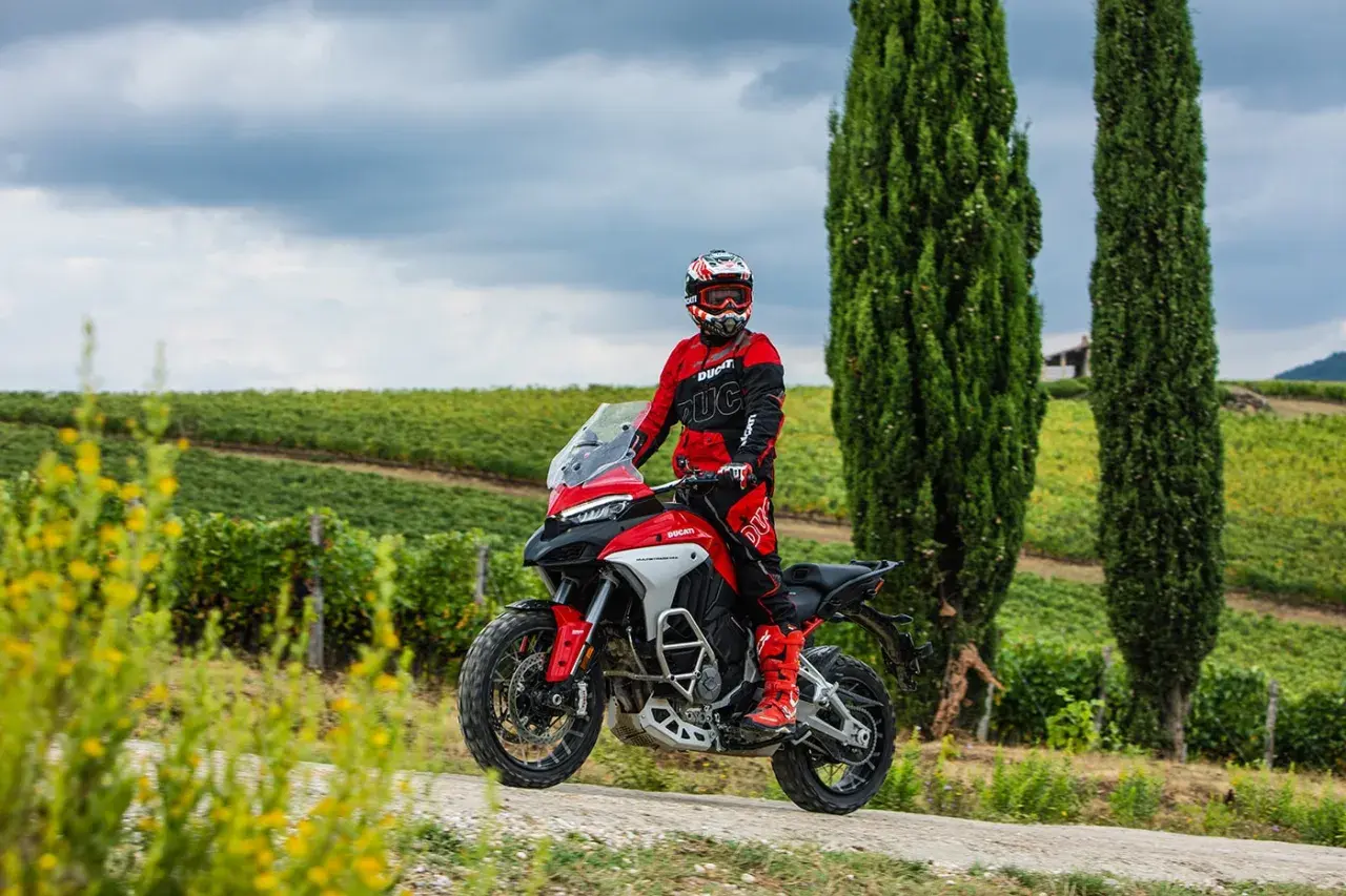 Un motociclista in tuta rossa sfreccia tra i vigneti toscani, godendosi le strade più belle della Toscana in moto.