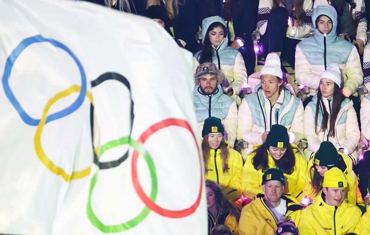 Młodzi sportowcy w barwach narodowych, z flagą olimpijską w tle, czekają na start reprezentacji Polski na Zimowe Igrzyska Olimpijskie 2026.
